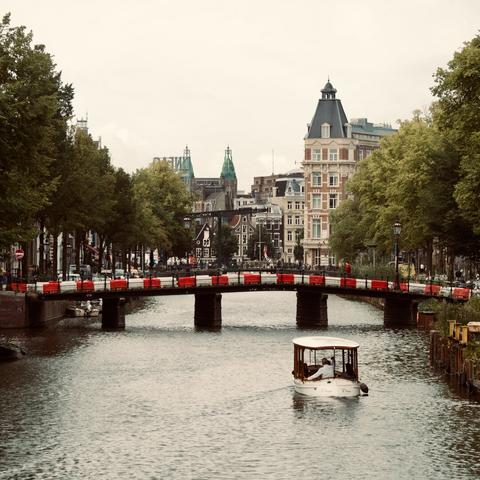 a canal with a small white boat, a bridge in the distance