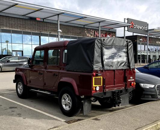 Maroon Land Rover Defender four-door pick-up, rear quarter view