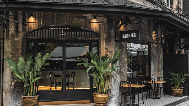 The exterior of a restaurant called "Sarnies," with plants, tables, and a rustic, aged aesthetic.