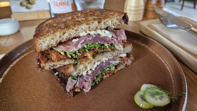 A sandwich on a brown plate with sliced pickles.
