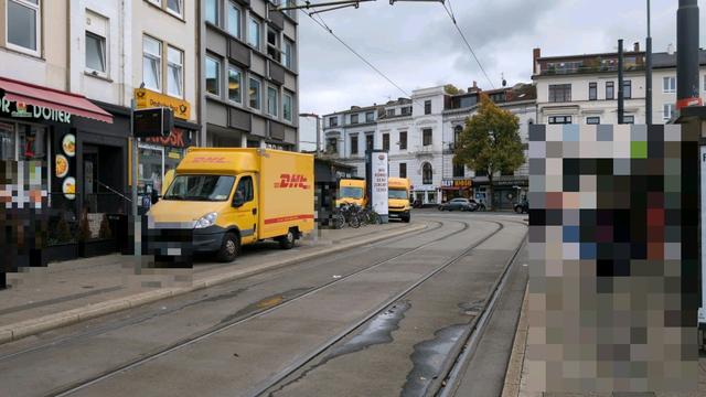 Drei DHL-Lieferwagen stehen gleichzeitig auf einer Straßenbahnhaltestelle vor einem Kiosk mit Paketshop.