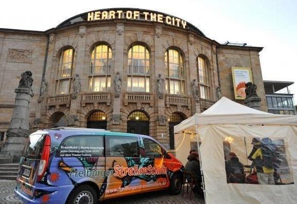 Sttassenschule van, bunt bemalt vor dem Stadttheater , auf dem Stadttheater steht der Schriftzug "heart oft the City" aus 2024