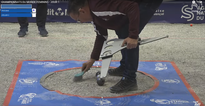 ein Schiri bürstet das Zielterrain mit einem Handbesen beim Präzisionsschießen im Petanque
