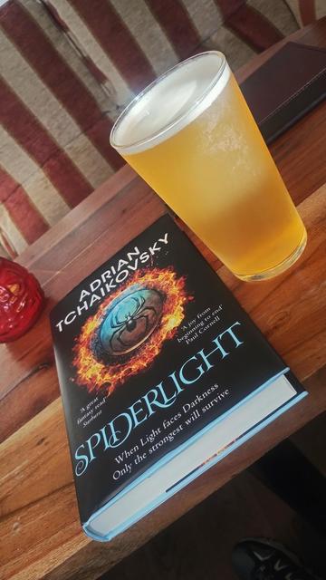Pint of amber coloured ale next to a hardback of Spiderlight by Adrian Tchaikovsky