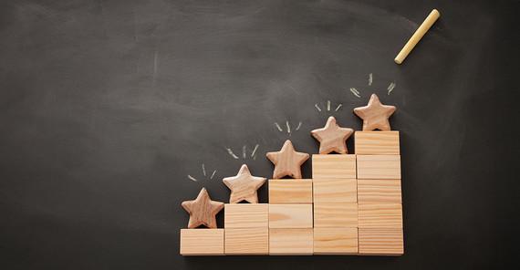 Das Bild ist ein Symbolbild zum Thema "Ranking" und zeigt insgesamt fünf Sterne aus Holz, einer jeweils auf einer Stufe eines fünfstufigen ansteigenden Siegertreppchens aus Holz. Das Foto stammt von AdobeStock/500380442_tomertu.