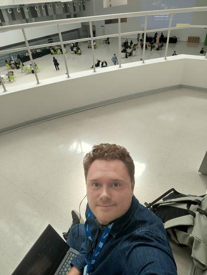 Mattias Axell taking a selfie at a balcony at the OGP Summit conference in Spain while holding a laptop and having his backpack behind him.
