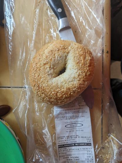 sobre una superficie de mosaico ocre descansa un bagel a medio partir. Debajo de él su bolsa revela una fecha: 18 de diciembre de 2022