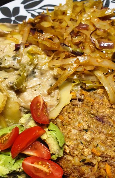 A plate with Walnut & oat burger, Potato and Leek Bake, Garlic, Chilli & Lime Sautéed Cabbage, fresh avocado and tomato.