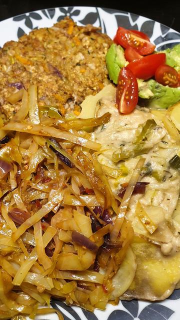 A plate with Walnut & oat burger; Potato and Leek Bake; Garlic, Chilli & Lime Sautéed Cabbage; fresh avocado and tomato.
