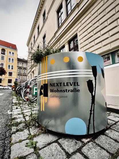 Ein großer Blumenkübel auf einer Straße auf dem steht Next Level Wohnstraße