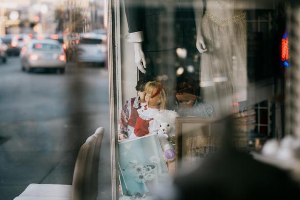 Dolls and mannequins peer out at a window at the traffic-filled streets.