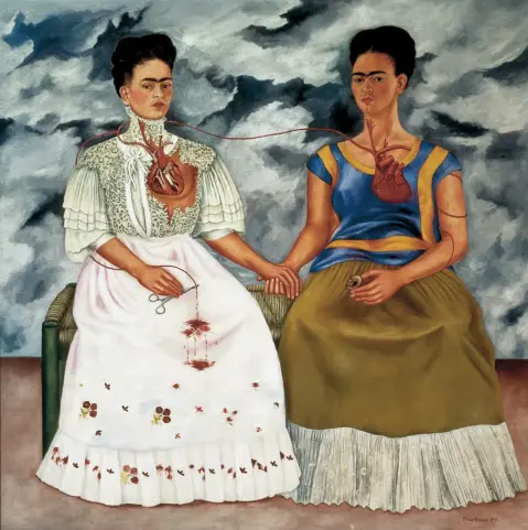 From Dr. Doris Maria-Reina Bravo, Smarthistory: “The double self-portrait The Two Fridas, 1939 features two seated figures holding hands and sharing a bench in front of a stormy sky. The Fridas are identical twins except in their attire, a poignant issue for Kahlo at this moment. The year she painted this canvas she was divorced from Diego Rivera, the acclaimed Mexican muralist. Before she married Rivera in 1929, she wore the modern European dress of the era, evident in her first self-portrait (left) where she dons a red velvet dress with gold embroidery. With Rivera’s encouragement, Kahlo embraced attire rooted in Mexican customs.“