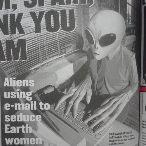 Photo of a 90s tabloid article showing an alien wearing a business suit while typing on a computer.  Aliens using e-mail to seduce Earth women EXTRATERRESTRIAL MESSAGE: Aliens have tapped to our Internet connections.