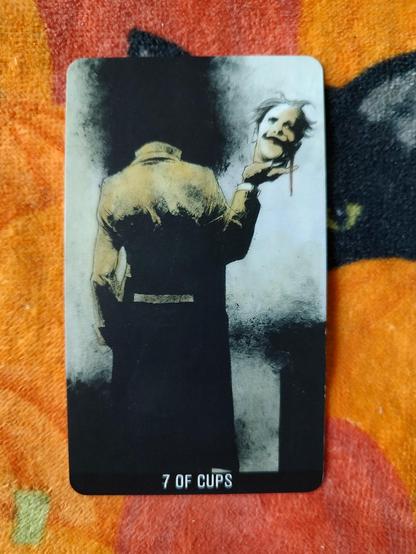 Card from the Joker Tarot deck. 
Seven of Cups.
A man, wearing a long coat, back the viewer, standing, with no head about the shoulders. He is holding his head on his right hand, the face facing the viewer somewhat smiling.
