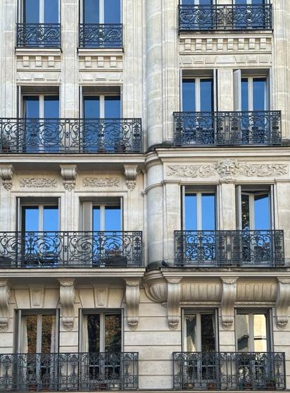 four floors of windows with ornate wrought-iron balconies on a beaux-arts-style building. The ironwork and stonemasonry vary with each floor.
