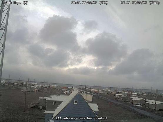 A webcam overseeing a beach with an ocean view, with a few small buildings and utility poles.