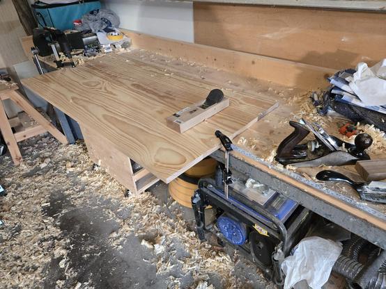 a table top clamped to my work bench.  it hangs over the edge by about a foot. a Japanese plane sits on top of the table top.  a Stanley #4 plane and some other tools sit off to the right.