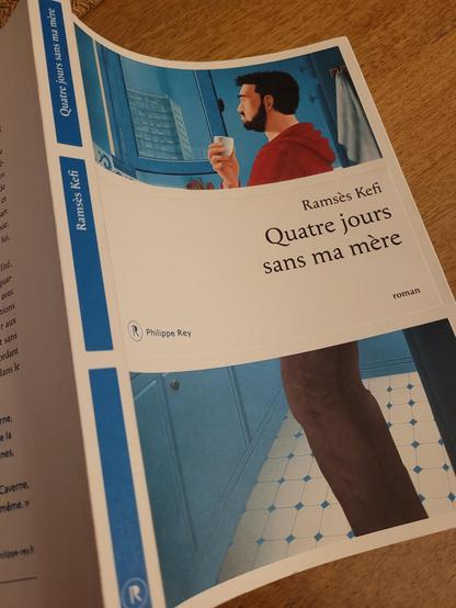 Couverture du livre de Ramsès Kefi, 4 jours sans ma mère, paru aux éditions Philippe Rey. La couverture dans les tons de bleus est un dessin montrant un homme portant un pull à capuche rouge regardant par la fenêtre un paysage d'immeuble.