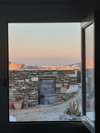 Sur une île des Cyclades, vue de la fenêtre de ma chambre sur le mur du perivoli qui abrite le citronnier du vent. Plus loin la montagne avec village tout blanc sur l'arête, et encore plus loin, le ciel rose et bleu