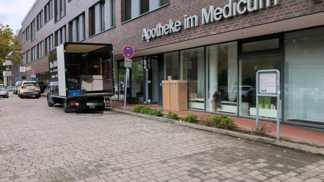 Ein Umzugswagen und zwei Taxen stehen im als Feuerwehrstellflävhe ausgeschilderten absoluten Haltverbot vor einem Ärztehaus. Auf dem schmalen Gehweg stehen Umzugskartons.