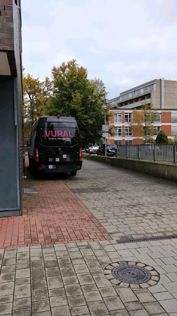 Ein Handwerker-Kastenwagen steht auf dem als Gehweg rot gepflasterten Teil einer Feuerwehrzufahrt eines Kranken- und Ärztehauses.