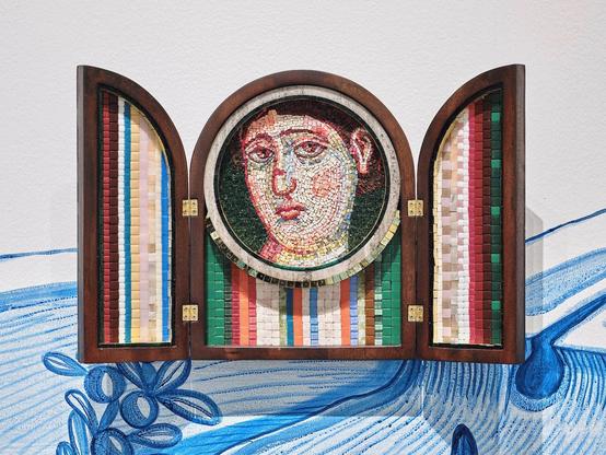 Image: Ursula Burke: Busted Nose, 2024, mosaic glass and custom mahogany frame, 58 x 37cm | this is a triptych in a wooden frame which is opened out; shut it would be the shape of a Roman arch, open it is two half-arches and a central arch; the semicircle of that arch becomes a circle which holds a mosaic of a face looking out at us quizzically; the lower part of the central panel and other panels in their totality are covered with colourful mosaic – patterned except for the face; the face has a red scar half way up the nose • “A solo exhibition by Ursula Burke Curated by Aoife Ruane • Run in association with the Highlanes Gallery    Siren is an expansive exhibition that incorporates ceramic sculpture, textile sculpture, tapestry and mosaic sculpture. Greco-Roman inspired, surrealist mosaic sculpture take centre stage framed by major new monumental tapestry work.    Having lived for over twenty years in post-conflict Belfast, during and after the peace process, Burke has developed…”