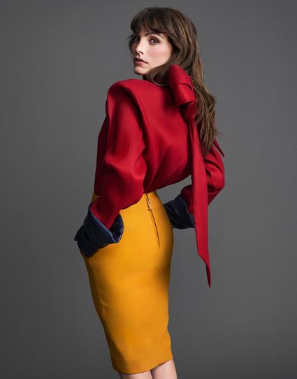 Lux Pascal lleva jersey con lazada de organza, falda lápiz en satén de seda y guantes de piel, todo de Saint Laurent X Anthony Vaccarello.