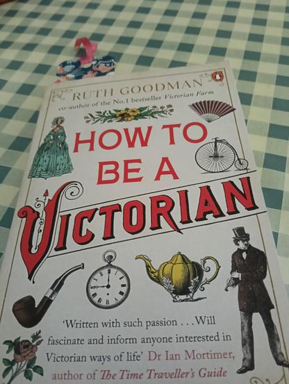 Un libro scritto da Ruth Goodman dal titolo "Hot ti be a Victorian" con in copertina un uomo e una donna stilizzati, una pipa, una teiera, un orologio da taschino, un ventaglio e una bici dell'epoca.