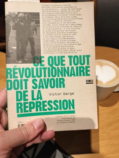 Couverture du livre "Ce que tout révolutionnaire doit savoir de la répression" de Victor Serge publié chez Zones. En arrière-plan, une tasse de café où un cœur est dessiné avec la mousse de lait est posée sur une table basse.