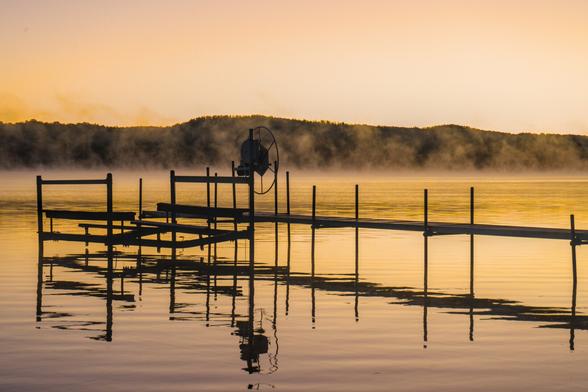 An image of a metal dock and boatlift in the morning light. Fog is blowing across the lake.