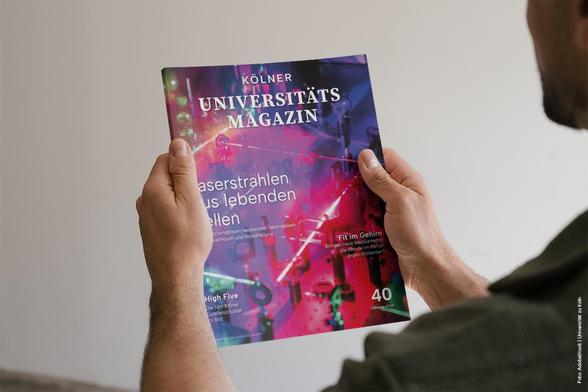 Person hält das Kölner Universitätsmagazin mit einem Titel über Laserstrahlen aus lebenden Zellen und Themen wie Fit im Gehirn und High Five. Ausgabe 40,