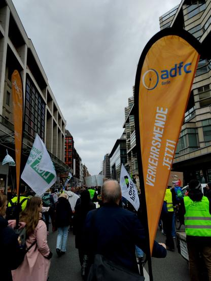 Foto einer strassenschlucht mit demonsttierenden Menschen, einige in warnwesten. Zentral rechts in Bild eine Beachflag mit Logo des adfc berlin und Slogan "verkehrswende jetzt"