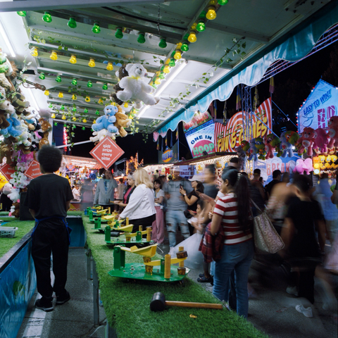 A chaotic whirl of motion around a game stall that features rubber mallets and small catapults on an astroturf ledge.