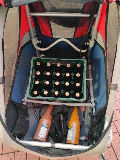 Ein Fahrradanhänger in dem eine Kiste Bier und zwei Flaschen Saft sind.