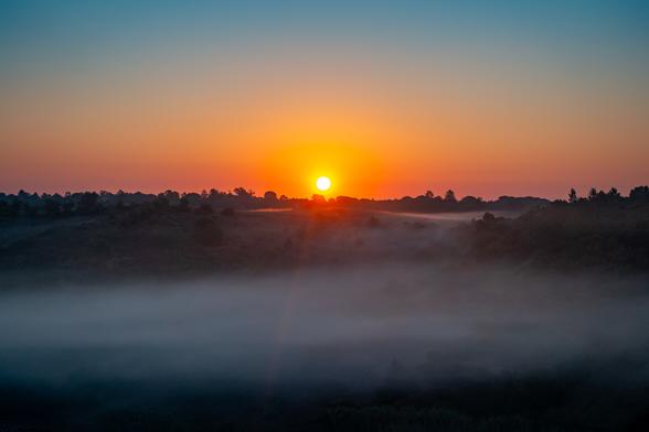 sun rising over hill with fog in the valley in front of it