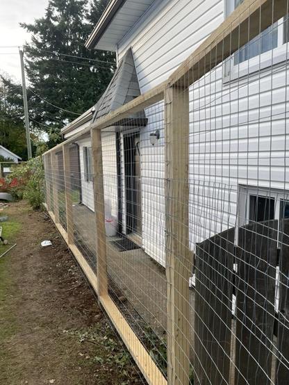 A tall wire fence extends into the distance beside a cement pathway beside a white house