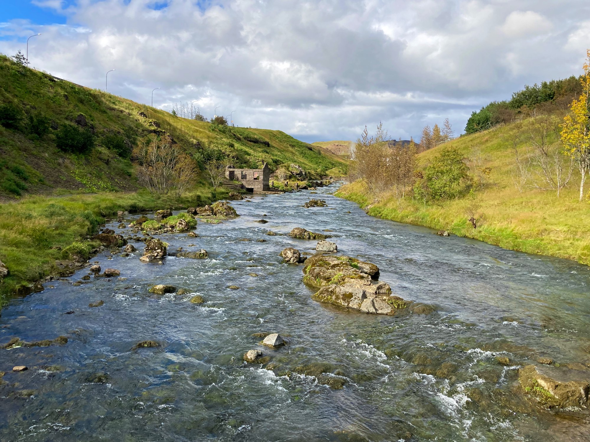 A tiny abandoned hydropower station next to a river surrounded by trees.