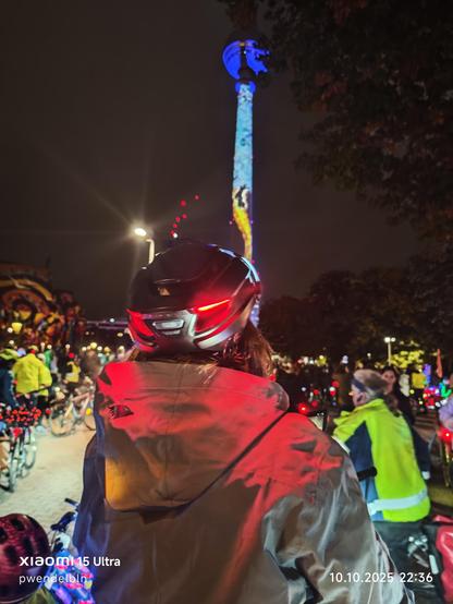 Am Ziel betrachten zahlreiche Radfahrer mit ihren blinkenden Fahrrädern den bunt beleuchteten Fernsehturm beim Festival of Lights