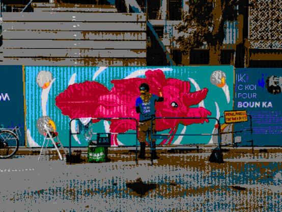 An artist painting an axolotl with bright colour, gear and protective railing in the middle of a grey street.