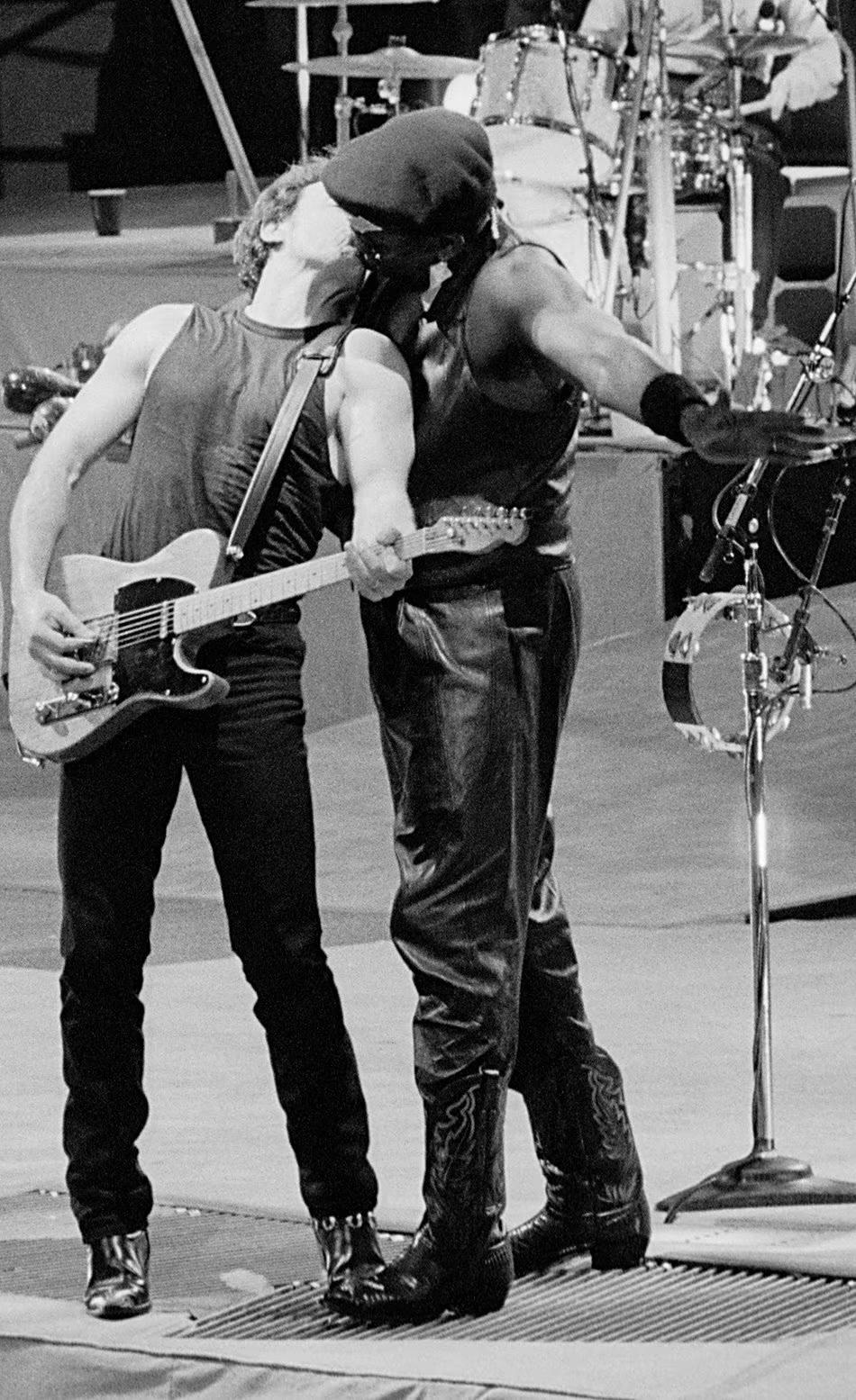 bruce is playing guitar and leaning back so that clarence can kiss him from behind