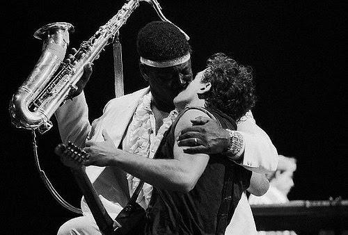 clarence holds a saxophone in one hand and bruce springsteen in the other while they kiss