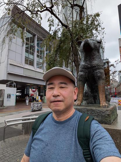 A selfie of a man in a white cap and the statue of Hachiko, the loyal dog