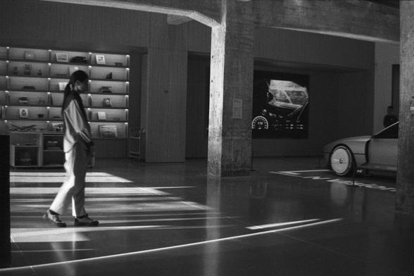 Ilford HP5 Plus 400 (FF)

English Alt Text:
A modern showroom with polished concrete floors and industrial-style pillars. A person walks across the space. On the left, shelves display books or merchandise, and a small cart is nearby. On the right, part of a sleek car is visible in front of a large digital screen showing futuristic vehicle graphics like a speedometer. The word “NIO” is printed on the floor, indicating this is an electric vehicle brand’s experience center.

中文替代文字：
一个现代展厅，地面为抛光混凝土，柱子呈工业风格。一人正从左向右走过。左侧墙上有展示书籍或商品的架子，旁边有一辆小推车。右侧可见一辆时尚汽车的部分，前方是一个大型数字屏幕，显示未来感十足的仪表盘图像。地板上印有“NIO”字样，表明这是一家电动车品牌的体验中心。