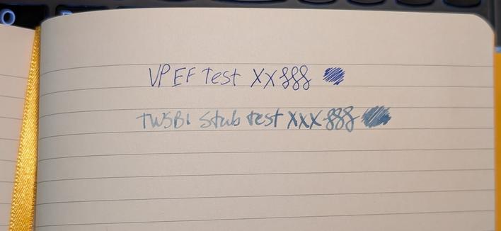 Photo of an open notebook. The paper is ivory with blue ruled lines. There is a yellow ribbon running down the spine.

Written on the paper are two lines:

"VP EF Test XX", three curlicues, and a scribble blob in dark blue ink.

"TWSBI Stub Test XXX", three curlicues, and a scribble blob in dark blue-gray ink.

Both lines show no sign of feathering. Both lines show some shading, there is significantly more shading on the second thicker line.
