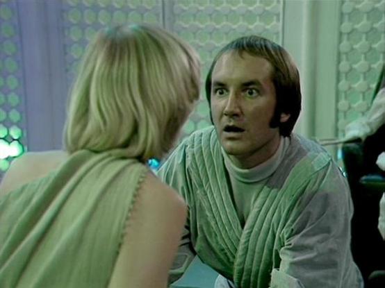 Claude Sonnet 4.0 describes the image as: "I can see this appears to be from a science fiction television series, showing two people in what looks like a futuristic interior setting with distinctive hexagonal or geometric patterns visible in the background. One person has blonde hair and is wearing what appears to be a light-colored garment, while the other person has dark hair and is wearing what looks like a ribbed or textured outfit in muted tones. The setting has a clinical or technological aesthetic typical of sci-fi productions from this era, with the geometric wall patterns and lighting creating an otherworldly atmosphere. However, I cannot identify the specific individuals in the image."

Blakes7Bot, version 3.9.33.