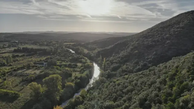 Un petit fleuve au pied d'un massif sous un ciel légèrement voilé. La lumière matinale vient illuminer l'eau du fleuve.