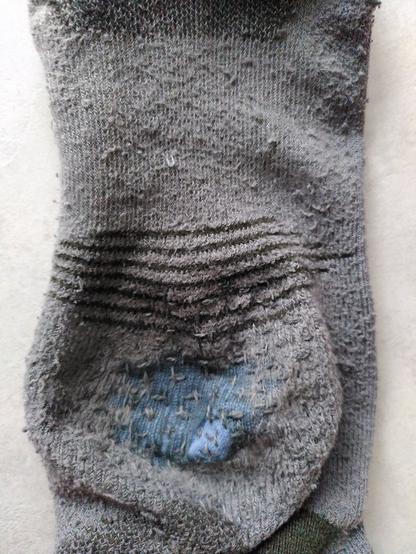 Photo of a grey sock which obviously had a hole in the heel, through which a blue patch fabric can be seen now, held in place by darning stitches.