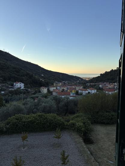 Piccolo paese ligure  in mezzo alle colline in fondo la costa e il mare con la luce azzurra e arancione del mattino