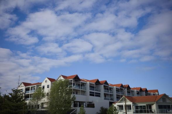 Auto-generated description: A series of white buildings with red roofs are set against a partly cloudy blue sky, surrounded by some trees.
