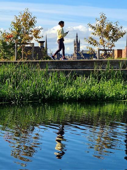 A canal with someone walking along the towpath, and the gothic tower of Glaagow University visible in the distance.